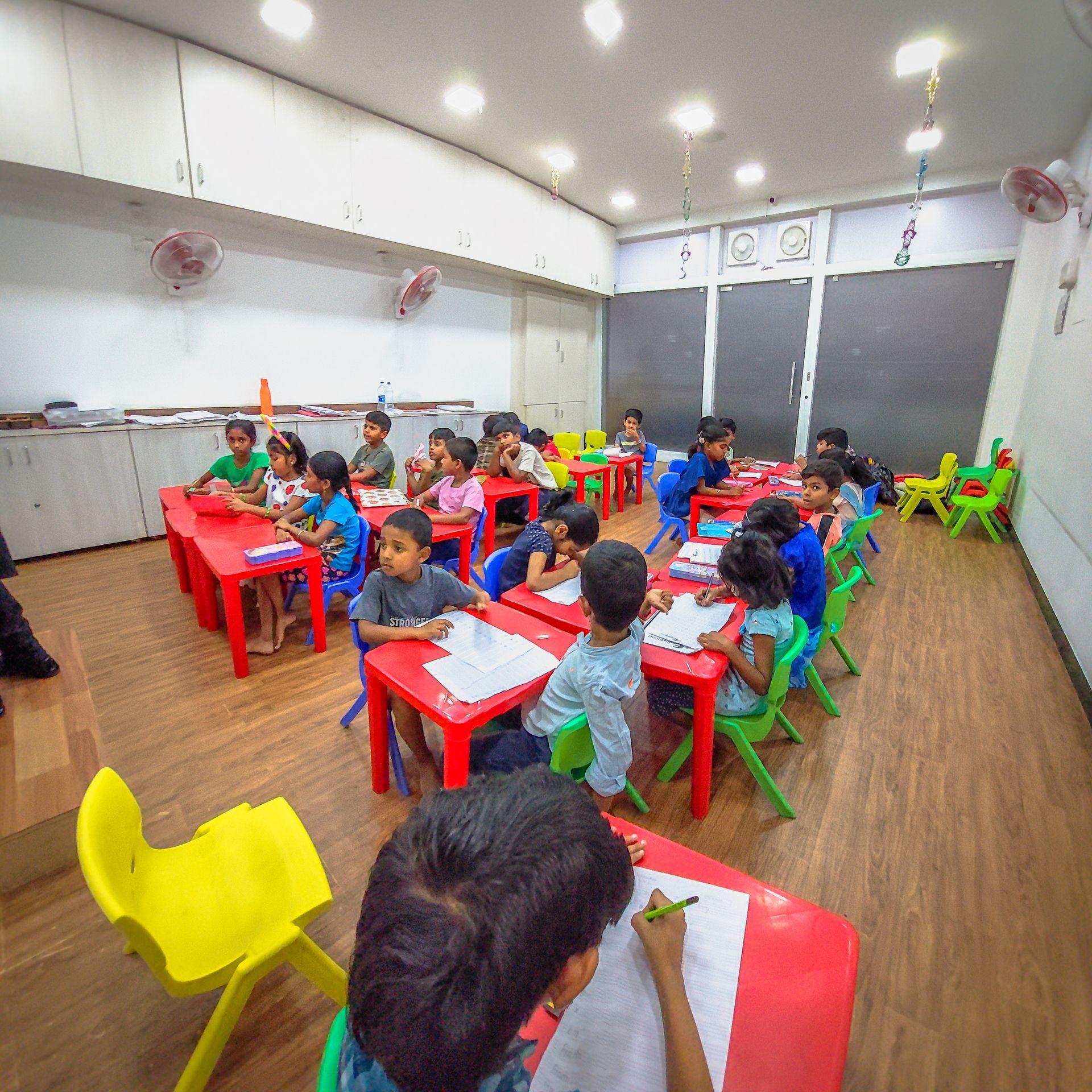 Children sitting at colorful desks in a classroom, engaged in writing activities.